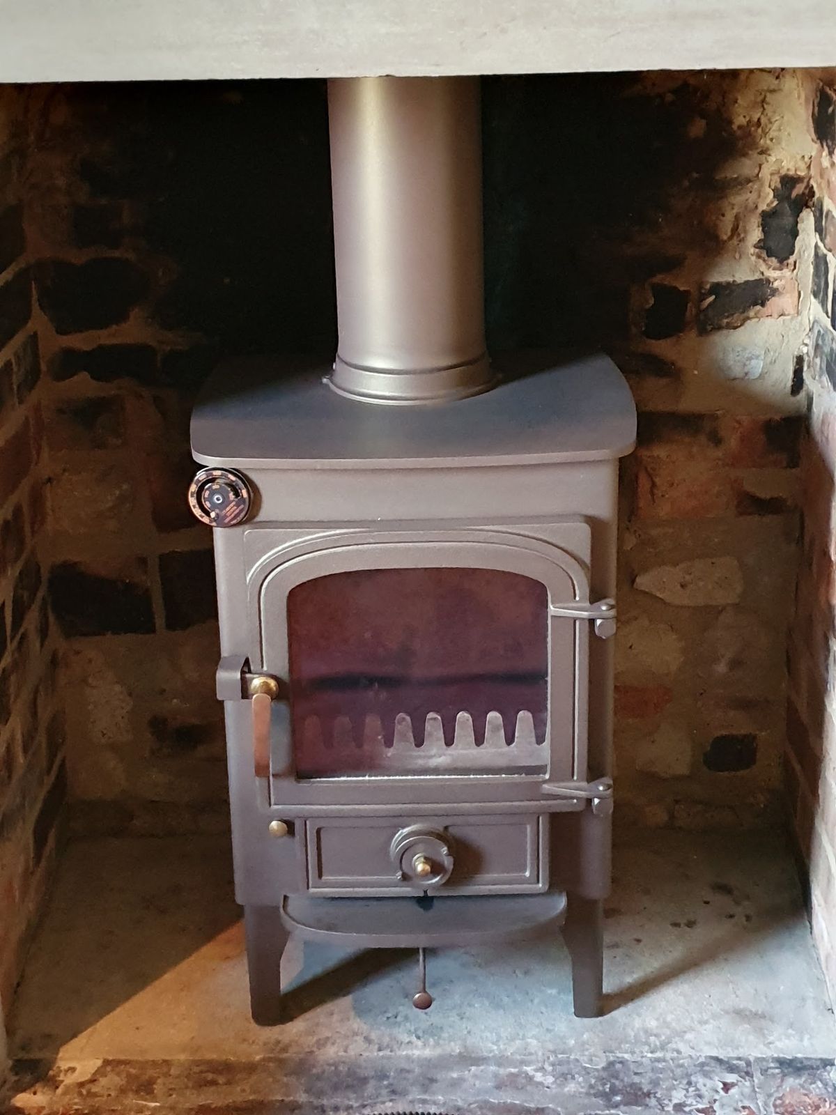 A grey stove with a tall flue in a stone and brick inglenook