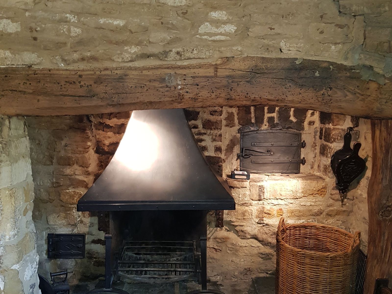An open fire with a black canopy in a stone and brick fireplace