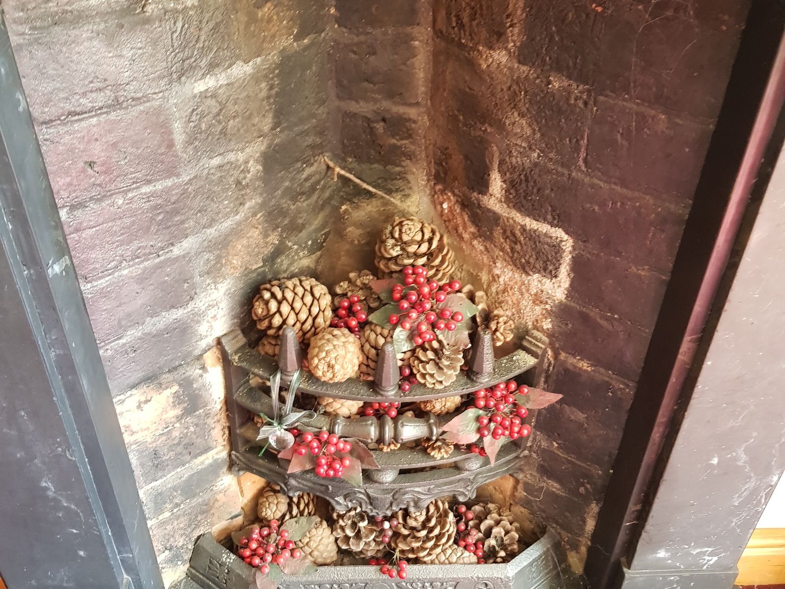 A small decorative fireplace filled with pine cones and berries